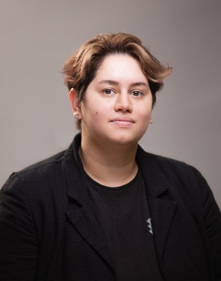 Headshot of Chloe wearing a black suit against a brown background